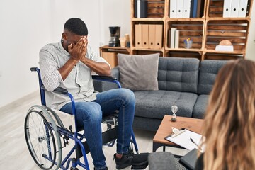 African american man doing therapy sitting on wheelchair with sad expression covering face with...