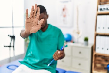 Obraz na płótnie Canvas Young african american man working at pain recovery clinic doing stop sing with palm of the hand. warning expression with negative and serious gesture on the face.
