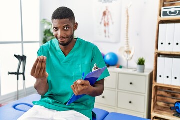 Young african american man working at pain recovery clinic doing money gesture with hands, asking...
