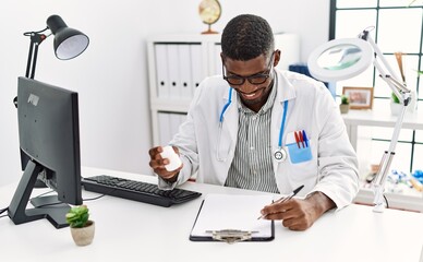 Young african american man wearing doctor uniform holding pills at clinic