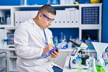 Young latin man scientist writing report working at laboratory