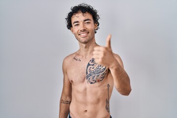 Fototapeta premium Hispanic man standing shirtless doing happy thumbs up gesture with hand. approving expression looking at the camera showing success.