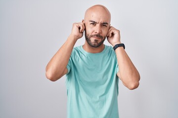 Fototapeta premium Middle age bald man standing over white background covering ears with fingers with annoyed expression for the noise of loud music. deaf concept.