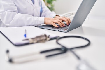 Fototapeta premium Young hispanic woman wearing doctor uniform using laptop working at clinic