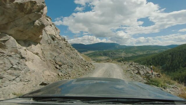 Car driving near stone cliff on a gravel road over precipice. SUV riding on country dirt road against mountains. Discovery and adventure travel concept. POV, onboard camera, sunny day 