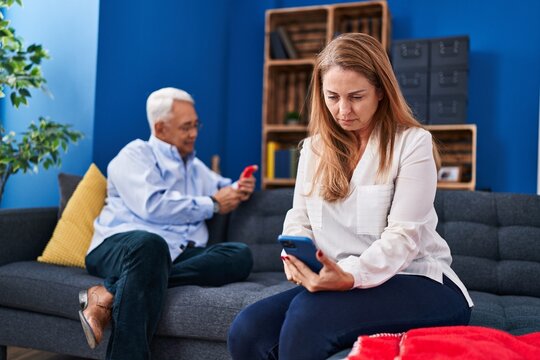 Middle Age Man And Woman Couple Using Smartphone Sitting On Sofa At Home