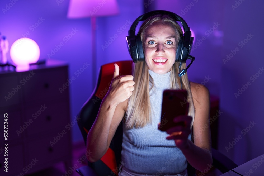 Sticker Young caucasian woman playing video games with smartphone smiling happy and positive, thumb up doing excellent and approval sign