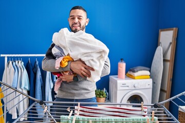 Hispanic man hanging clothes at clothesline winking looking at the camera with sexy expression,...
