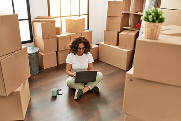 Fototapeta premium Middle age hispanic woman smiling confident using laptop at new home