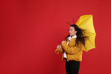 Woman with umbrella caught in gust of wind on red background. Space for text