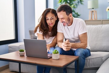 Middle age man and woman couple using laptop sitting on sofa at home