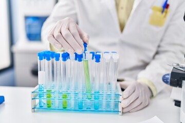 Fototapeta premium Young hispanic man wearing scientist uniform holding test tubes at laboratory
