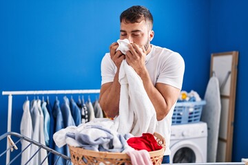 Young hispanic man smelling towel hanging clothes on clothesline at laundry room