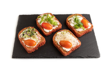 Red beet bread sandwiches with tomatoes and microgreen on black board isolated on white. side view.