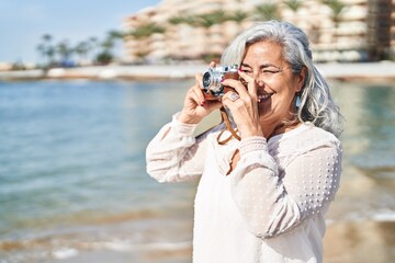 Middle age woman smiling confident using professional camera at seaside