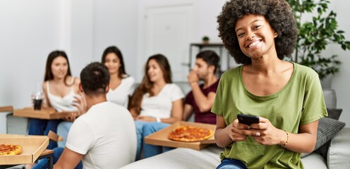 Group of young friends eating italian sitting on the sofa. Woman smiling and using smartphone at home.