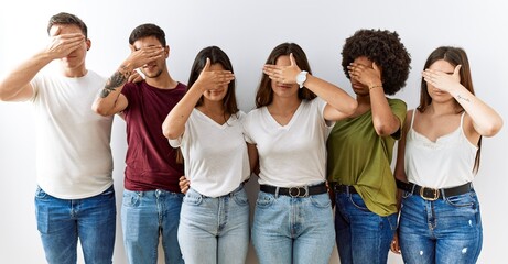 Group of young friends standing together over isolated background covering eyes with hand, looking serious and sad. sightless, hiding and rejection concept
