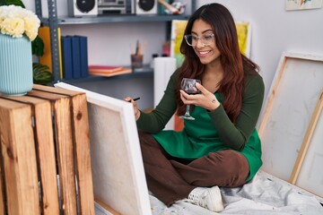 Young hispanic woman artist drawing and drinking wine at art studio
