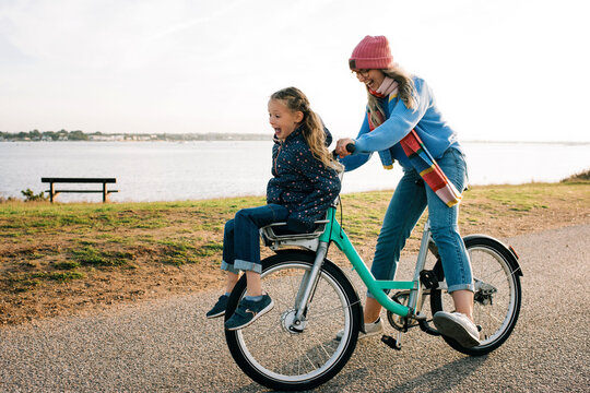 mother and daughter cycling on a hire bike laughing at the beach