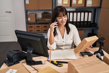 Young beautiful hispanic woman ecommerce business worker talking on smartphone holding package at office