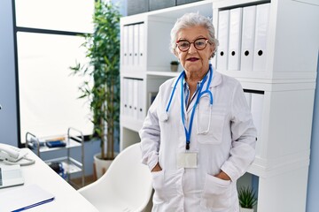 Senior grey-haired woman wearing doctor uniform standing at clinic