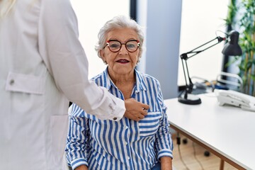 Senior grey-haired woman patient having medical consultation auscultating heart at clinic
