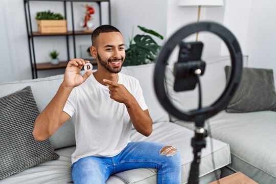 African american man recording vlog tutorial about bitcoin with smartphone at home smiling happy pointing with hand and finger