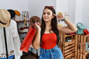 Young brunette woman holding shopping bags at retail shop smiling pointing to head with one finger, great idea or thought, good memory