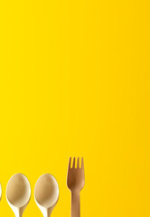 plastic spoons and a wooden cutlery, on a yellow background
