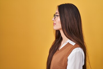 Young brunette woman standing over yellow background wearing glasses looking to side, relax profile pose with natural face with confident smile.