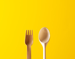 wooden fork and plastic spoon, yellow background
