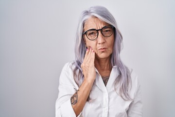 Middle age woman with tattoos wearing glasses standing over white background touching mouth with hand with painful expression because of toothache or dental illness on teeth. dentist