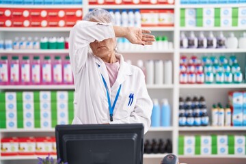 Middle age woman with tattoos working at pharmacy drugstore covering eyes with arm, looking serious and sad. sightless, hiding and rejection concept