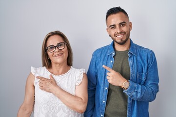 Hispanic mother and son standing together cheerful with a smile on face pointing with hand and...