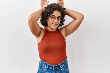 Young hispanic woman wearing glasses standing over isolated background doing bunny ears gesture with hands palms looking cynical and skeptical. easter rabbit concept.