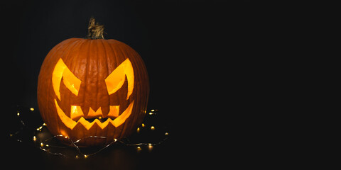 Real Halloween orange pumpkin in black background with fairy lights giving spooky season vibes. Scary pumpkin head portrait glowing inside with orange lights, October 16, 2022.