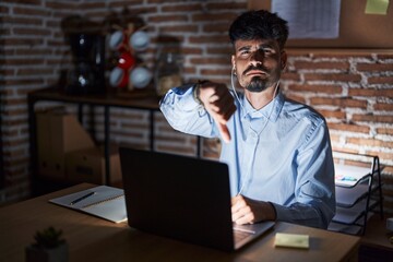 Fototapeta na wymiar Young hispanic man with beard working at the office at night looking unhappy and angry showing rejection and negative with thumbs down gesture. bad expression.