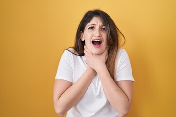Naklejka premium Young brunette woman standing over yellow background shouting and suffocate because painful strangle. health problem. asphyxiate and suicide concept.