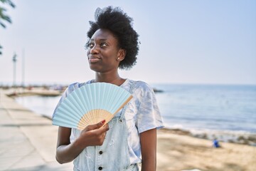 Young african woman using hand fan by the sea