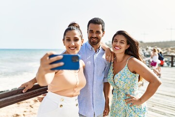 Three young hispanic friends smiling happy make selfie by the smartphone at the beach.