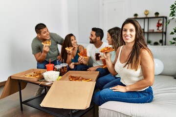 Group of young hispanic friends smiling happy eating italian pizza sitting on the sofa at home.