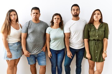 Group of young hispanic friends standing together over isolated background puffing cheeks with funny face. mouth inflated with air, crazy expression. - obrazy, fototapety, plakaty