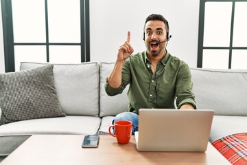 Young hispanic man with beard wearing call center agent headset working from home pointing finger up with successful idea. exited and happy. number one.