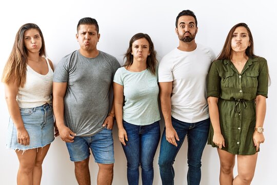 Group of young hispanic friends standing together over isolated background puffing cheeks with funny face. mouth inflated with air, crazy expression.