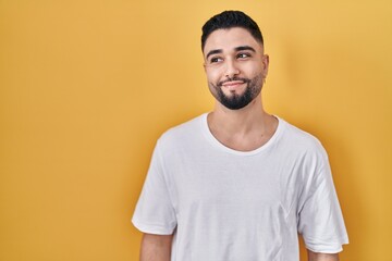 Young handsome man wearing casual t shirt over yellow background smiling looking to the side and staring away thinking.