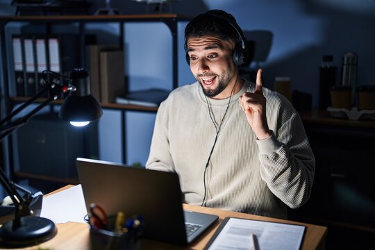 Young handsome man working using computer laptop at night pointing finger up with successful idea. exited and happy. number one.