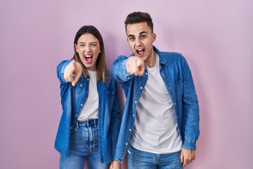 Fototapeta na wymiar Young hispanic couple standing over pink background pointing displeased and frustrated to the camera, angry and furious with you