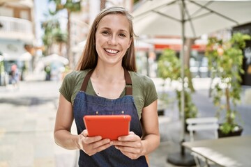 Young blonde woman wearing apron using touchpad at coffee shop