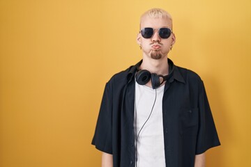 Young caucasian man wearing sunglasses standing over yellow background puffing cheeks with funny face. mouth inflated with air, crazy expression.