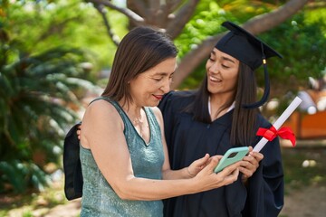 Two women mother and graduated daughter using smartphone at park